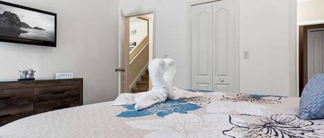 Une chambre à coucher avec un lit, une commode, un tableau encadré et un escalier menant à une autre pièce.