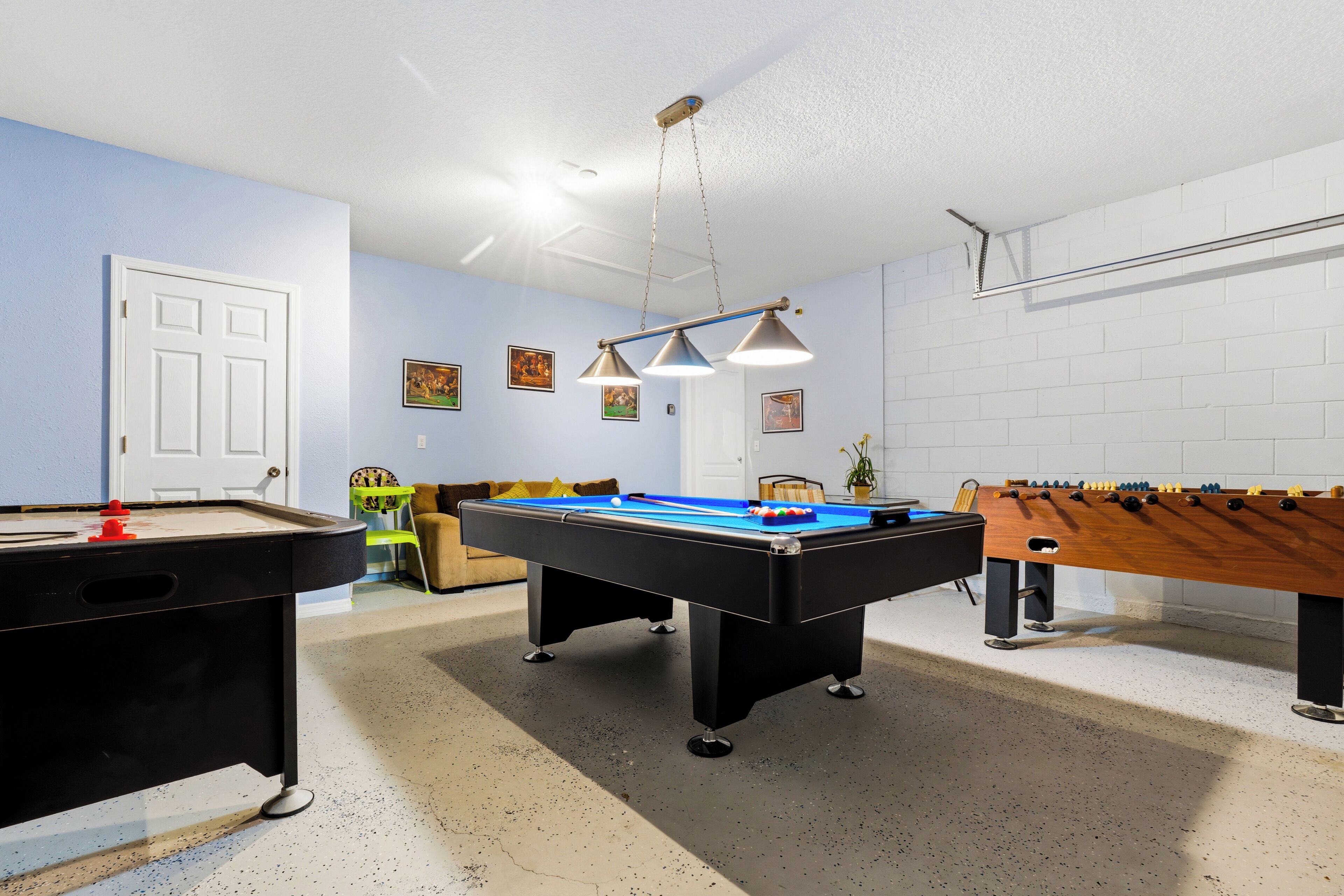 A pool table, foosball table, and a sofa in a room with a white door and light blue walls.