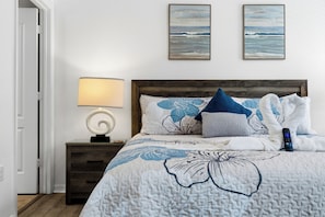 A neatly made bed with a floral-patterned bedspread, a bedside lamp, and two framed pictures on the wall.