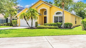 A yellow house with a garage, surrounded by well-maintained lawns and palm trees. - Allamanda Holiday Home 4 Bedroom (Kissimmee)