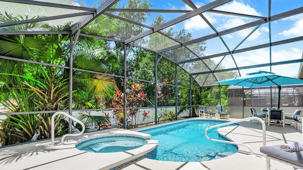 A swimming pool with a hot tub, surrounded by lush tropical plants and a covered seating area. - Allamanda Holiday Home 4 Bedroom (Kissimmee)