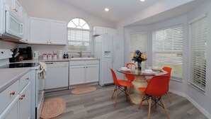 Een moderne keuken met witte kasten, een inbouwoven, een vaatwasser en een eethoek met een ronde tafel en oranje stoelen.