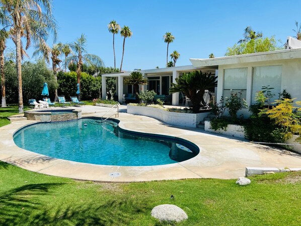 Relax by the pool surrounded by lush greenery and palm trees, with lounge chairs and a covered seating area.
