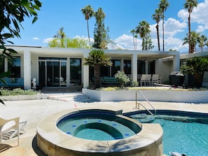 A modern outdoor pool area with a hot tub, lounge chairs, and palm trees.