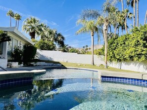 Relax by the serene pool surrounded by lush greenery and palm trees.