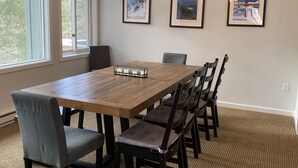 Un comedor con una mesa de madera, seis sillas, una araña y tres carteles enmarcados en la pared.