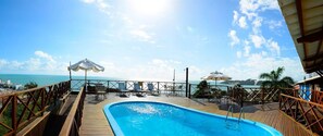 A pool area with a view of the ocean, deck chairs, umbrellas, and a wooden deck. - Marsallis Ponta Negra Hotel (Natal)