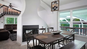Un salón espacioso con chimenea, un comedor con mesa y sillas de madera, y un ventanal con vistas al exterior.