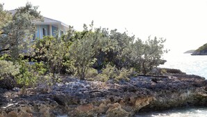 Una propiedad costera con terreno rocoso, un edificio con columnas y vegetación densa.