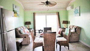 Una sala de estar con una mesa de comedor, sillas de mimbre, un sofá, un refrigerador y un ventilador de techo.