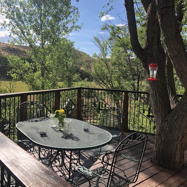 A patio with a round metal table and chairs, surrounded by a wooden deck and metal railing. - Beautiful creek side log home, lots of open space but only minutes to town. (New Castle)