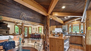 L’intérieur d’un chalet rustique comprend un coin repas, une cuisine et une grande structure en bois apparent.