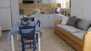 Een compacte keuken met een eettafel en stoelen, een bank en een raam met uitzicht op groen.