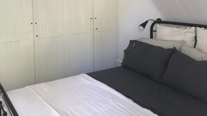 Een slaapkamer met een bed, een bedlampje, een witte kledingkast en een hangende lamp.
