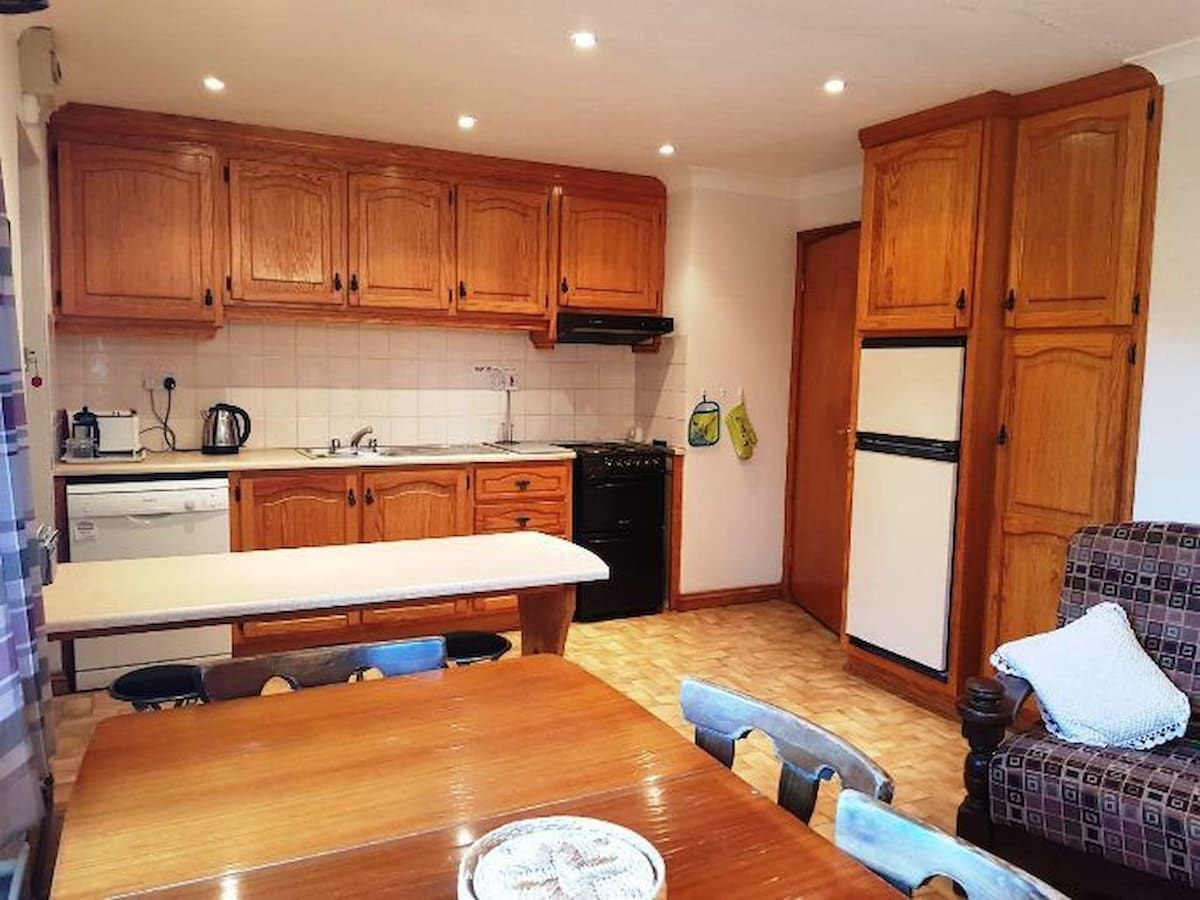 A compact kitchen with wooden cabinets, a dining table, and a refrigerator.