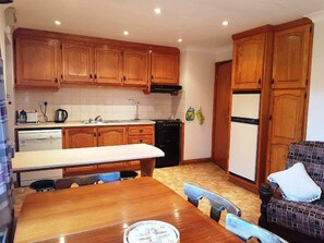 A compact kitchen with wooden cabinets, a dining table, and a refrigerator.