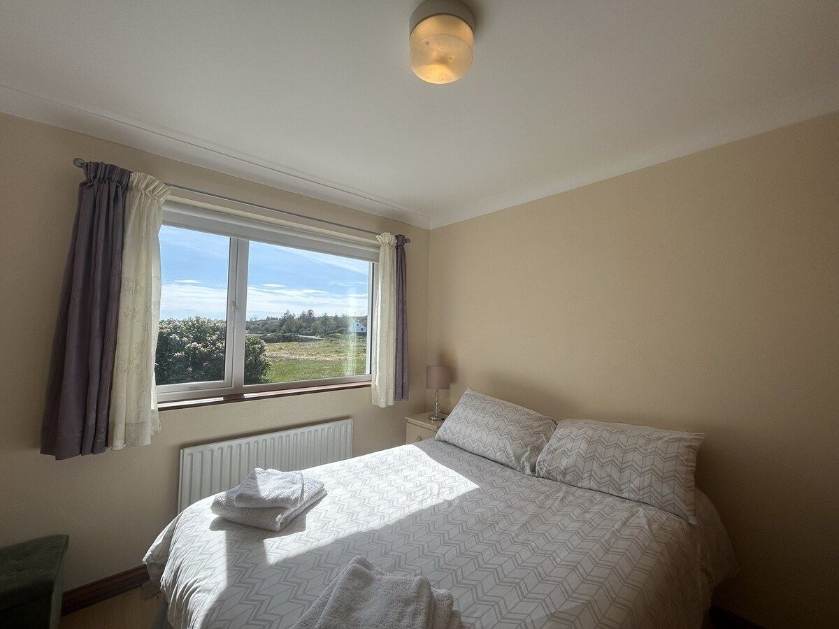 A bedroom with a bed, a window with curtains, a bedside lamp, and a radiator.