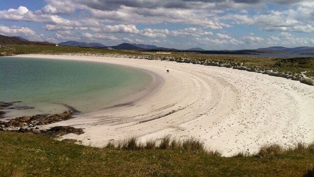 A coastal landscape with a sandy beach, a clear blue sea, and distant mountains under a partly cloudy sky. - Waterside Cottage stunning sea & mountain views. (Connemara)