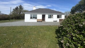 A single-story house with a gravel driveway, a front door, and a small porch. - Waterside Cottage stunning sea & mountain views. (Connemara)