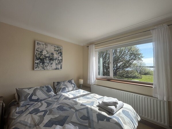 A bedroom with a bed, a window with curtains, a radiator, and a wall-mounted painting.
