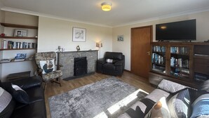 A living room with a fireplace, a television, and a bookshelf. - Waterside Cottage stunning sea & mountain views. (Connemara)