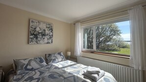 A bedroom with a bed, a window with curtains, a radiator, and a painting on the wall. - Waterside Cottage stunning sea & mountain views. (Connemara)