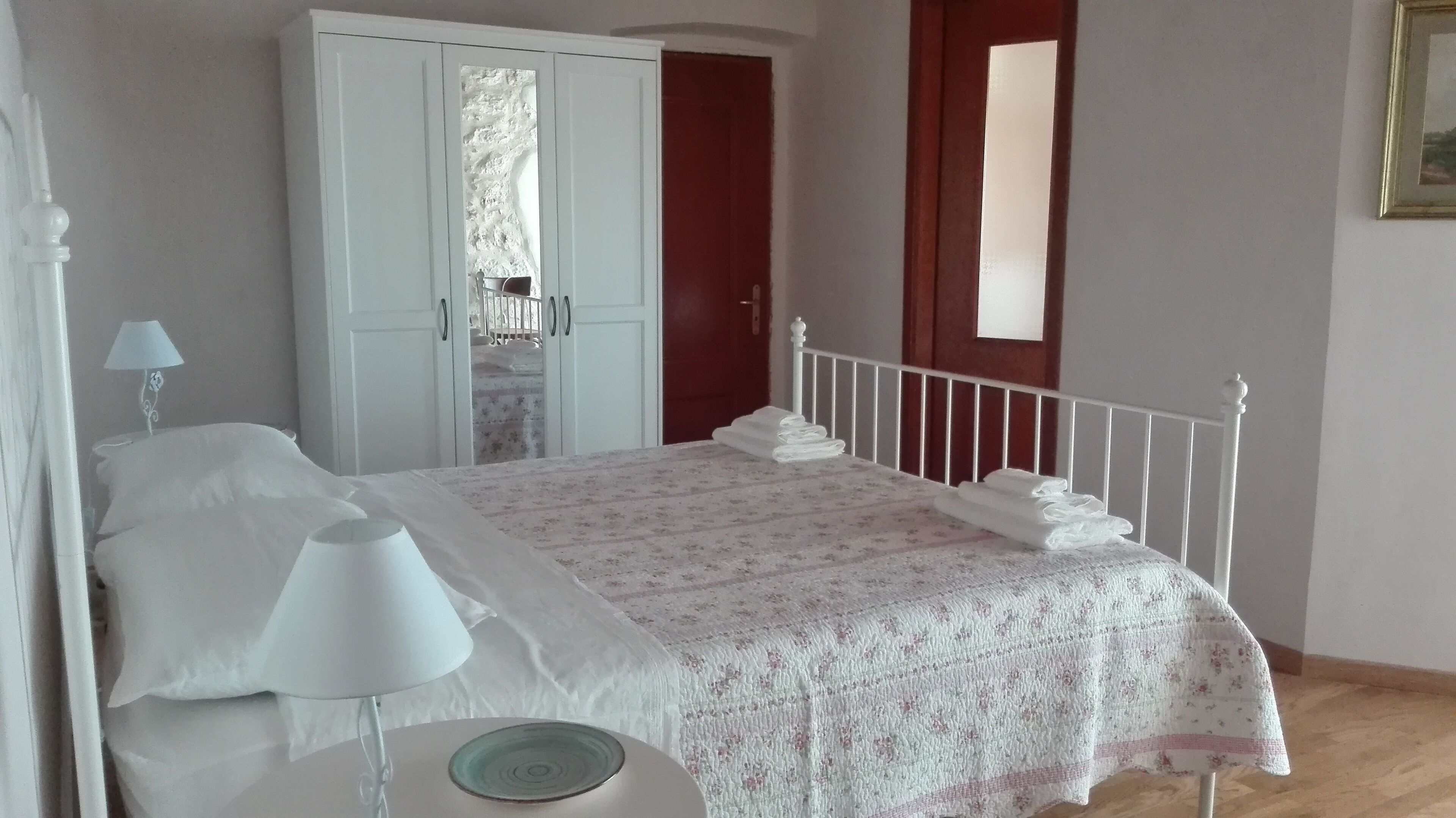 Quarto com cama, mesa de cabeceira, abajur, guarda-roupa e janela.