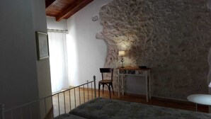 A bedroom with a stone wall, a bed, a desk with a lamp, and a chair. - Small Alvitano shelter (Alvito, Frosinone)