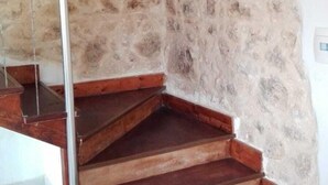 A staircase with wooden steps and a metal handrail, leading to a landing with a white wall and a stone wall with a rough texture. - Small Alvitano shelter (Alvito, Frosinone)