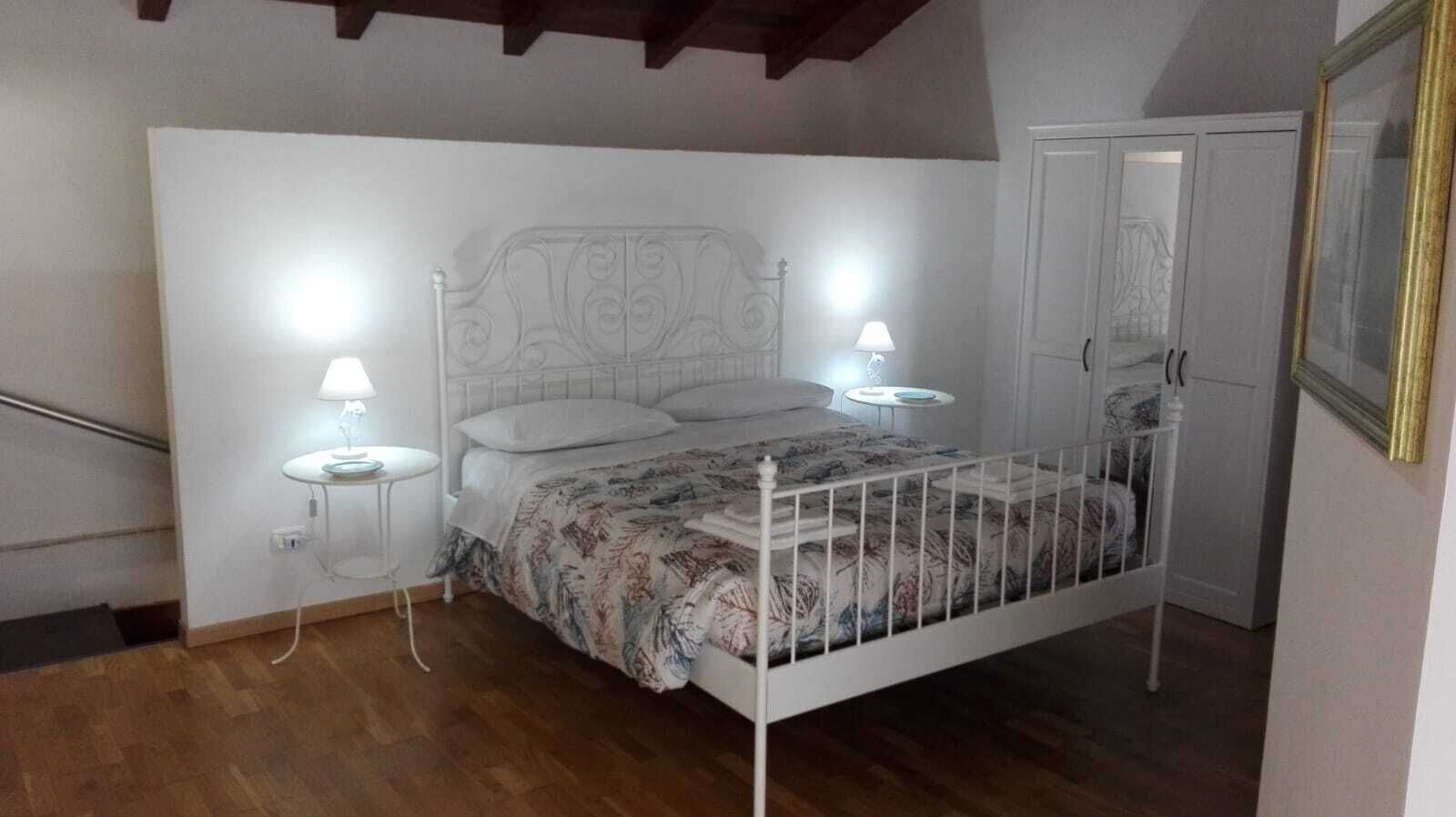 Un dormitorio con una cama, dos lámparas de noche, una mesita y un armario.