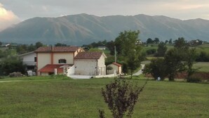 A rural house with a red-tiled roof, surrounded by a grassy field and mountains in the background. - Small Alvitano shelter (Alvito, Frosinone)