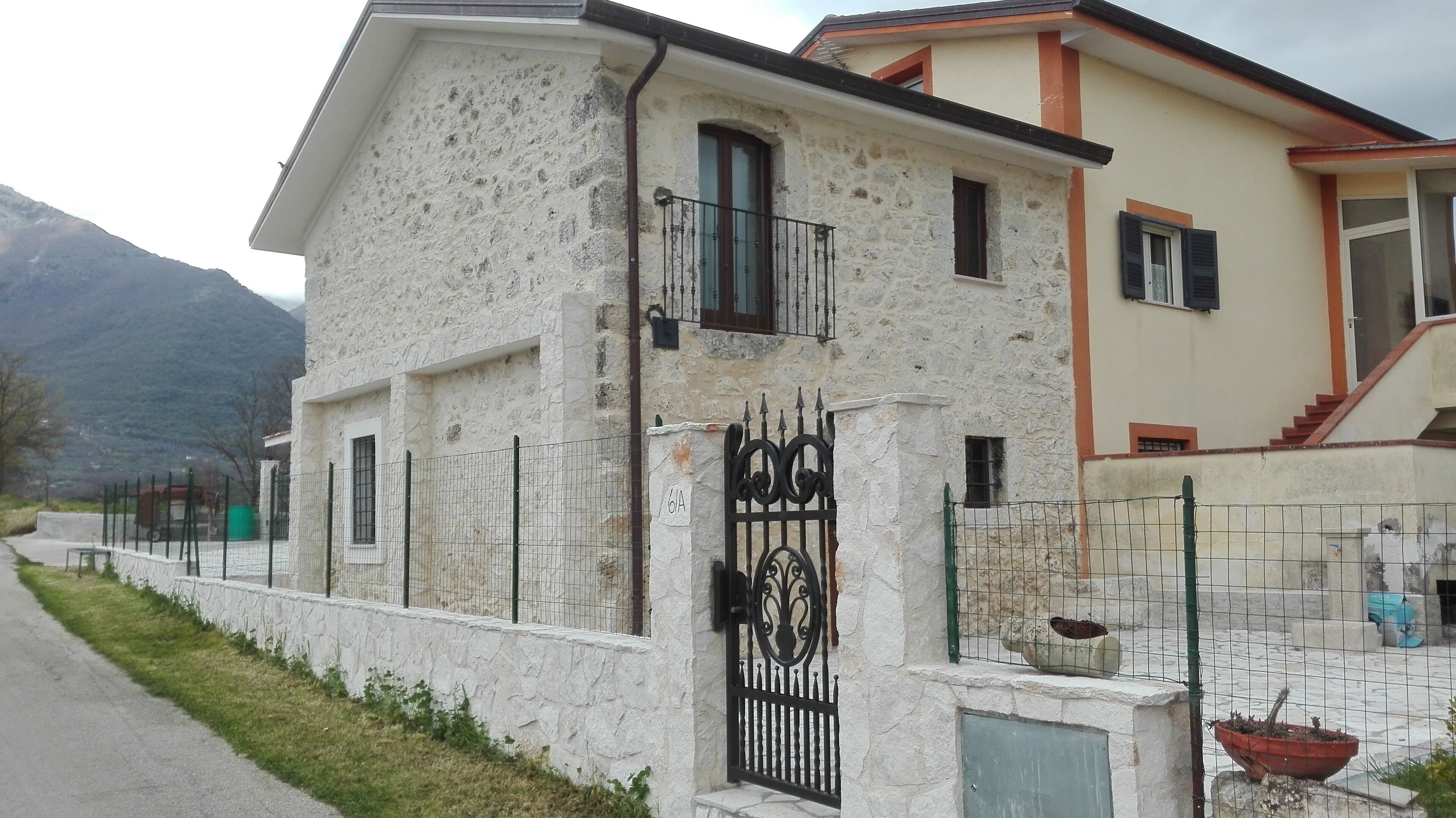 A two-story building with a stone facade, a gated entrance, and a small balcony.
