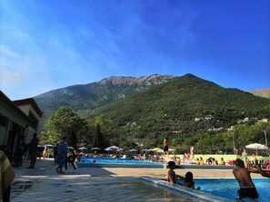 A pool area with a mountain backdrop, surrounded by umbrellas and people. - Small Alvitano shelter (Alvito, Frosinone)