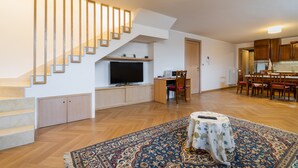 A spacious living area with a wooden staircase, a flat-screen TV, a dining table, and a patterned rug. - Newly built villa: Car garage, 3 bedrooms, 6p let, large kitchen, gardens (Tuglie)