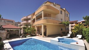 Edificio de dos pisos con un área de piscina, que incluye un jacuzzi y sillas de descanso.