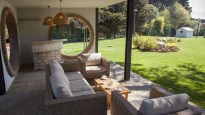 An outdoor patio with wicker furniture, a stone fireplace, and a view of the garden.