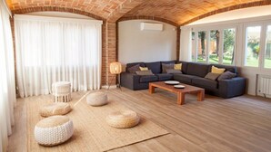 A living room with a brick ceiling, a grey sofa with cushions, a wooden coffee table, and woven poufs on a woven rug.