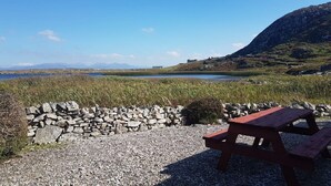 Une table de pique-nique et un muret de pierre au bord d’un lac, avec une montagne en arrière-plan.