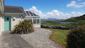 Une maison dotée d’une véranda, d’une allée en gravier et offrant une vue sur un lac et des montagnes.