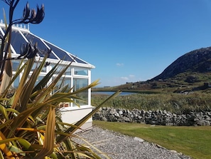 Un bâtiment moderne doté de grandes fenêtres, d’un mur en pierre et offrant une vue sur un lac et des collines.