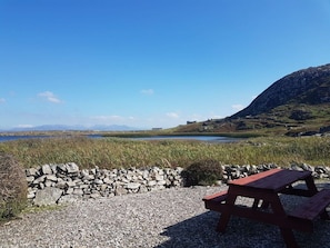 Un espace pique-nique agrémenté d’un muret en pierre et d’une table en bois, offrant une vue sur un lac et, au loin, sur des montagnes.