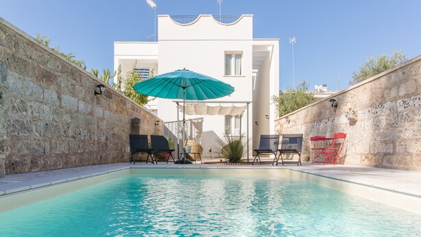 A swimming pool with lounge chairs and umbrellas, surrounded by stone walls and a white building in the background. - Salento Rosa dei Venti - Scirocco (Surbo)