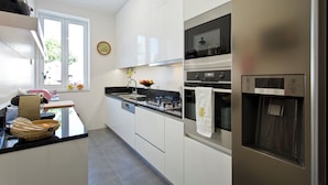 Una cocina moderna con armarios blancos, un refrigerador de acero inoxidable y una ventana con vistas a la vegetación.