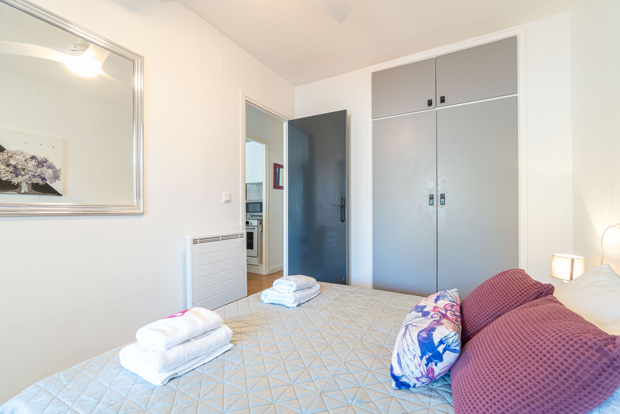 A bedroom with a bed, a wardrobe, a mirror, and a wall-mounted picture.