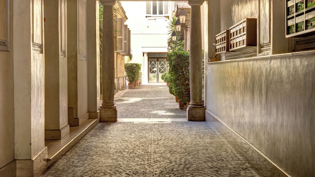 A cobblestone alleyway with classical architecture, including columns and a covered entrance. - Rome Boutique Apartments with terrace, whirlpool in room, central.   (6900335)