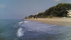 A beach with waves, a sandy shore, and buildings in the background.