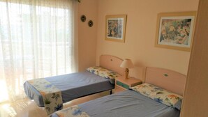A room with two beds, a nightstand with a lamp, and two framed pictures on the wall.