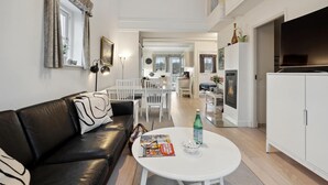 A modern living room with a black leather sofa, white dining table, and a white cabinet with a television.