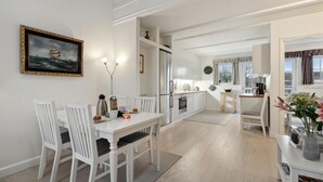 A modern kitchen with white cabinetry, a dining area with white chairs, and a view of the outside through the windows.