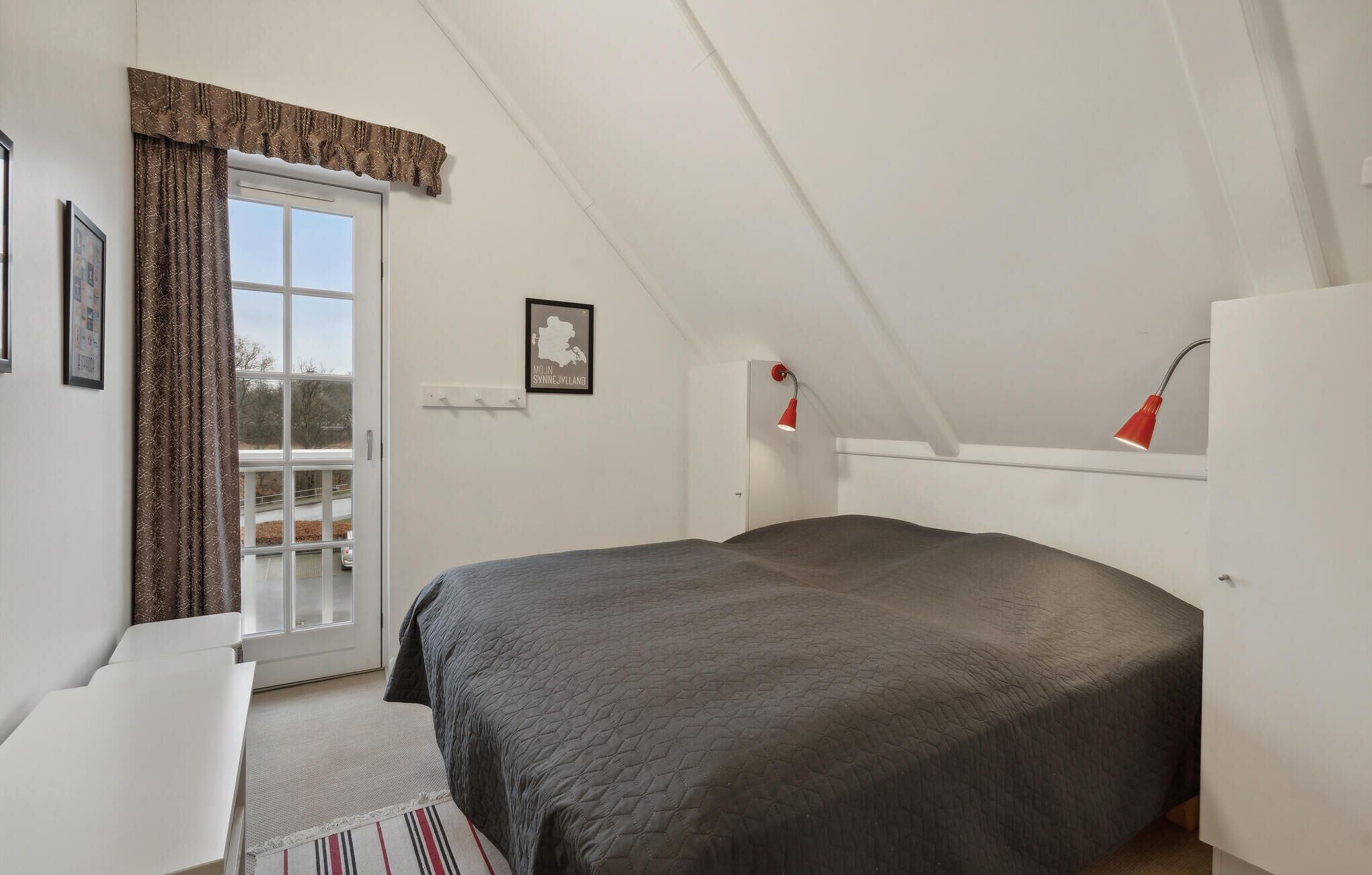 Ein Schlafzimmer mit Bett, Schreibtisch, Stuhl, einem Fenster mit Vorhängen und einer Karte an der Wand.
